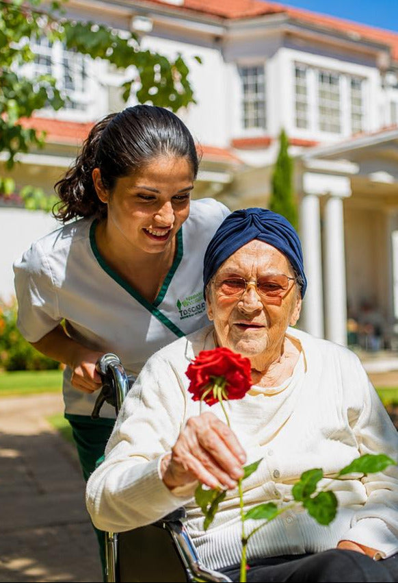 Cuidadora acompañando a una residente en el jardín de La Toscana
